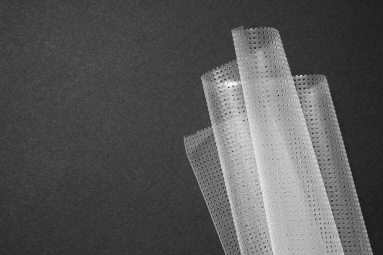 bioaqualife: A close-up of a translucent sheet of bubble wrap against a dark background. The bubbles are evenly spaced, creating a textured pattern. The material is rolled and partially unfurled, with light reflecting off the surface.