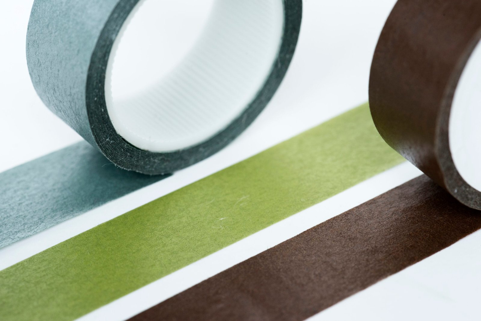 bioaqualife: Close-up of three rolls of adhesive tape in gray, green, and brown, each next to a matching strip of tape laid out flat on a white surface.