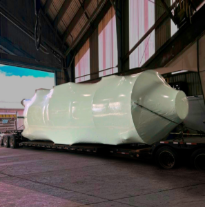bioaqualife: A large, cylindrical object wrapped in white protective material is secured on a flatbed trailer inside an industrial warehouse with high ceilings and large windows.