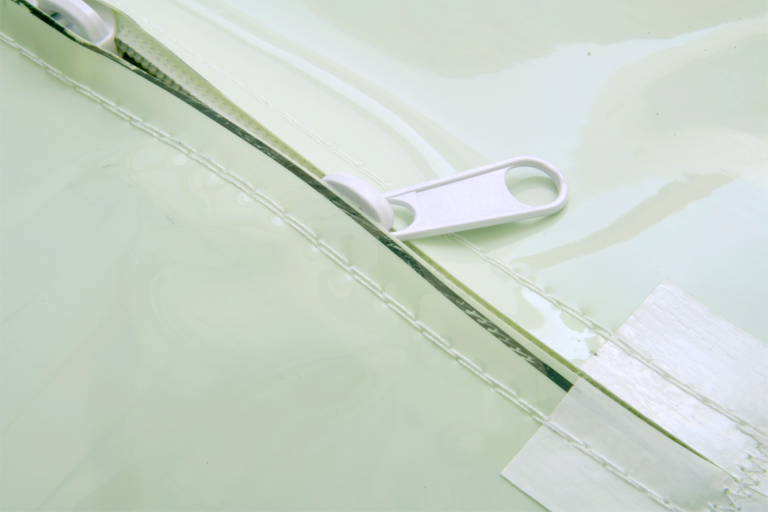bioaqualife: A close-up of a white zipper partially open on a shiny, pale green surface with white tape applied nearby.