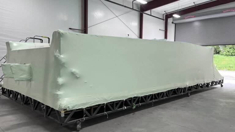 bioaqualife: A large, rectangular object wrapped in pale green protective plastic sits on a metal frame inside an industrial warehouse with concrete floors and an open garage door.