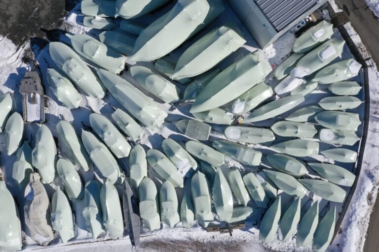 bioaqualife: Aerial view of numerous boats covered in protective wraps and arranged closely together in a snow-covered outdoor storage area near a building.