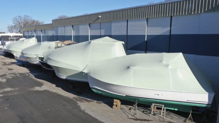 bioaqualife: Several boats covered in pale green protective shrink wrap are lined up on stands outside a large metal building on a clear day.