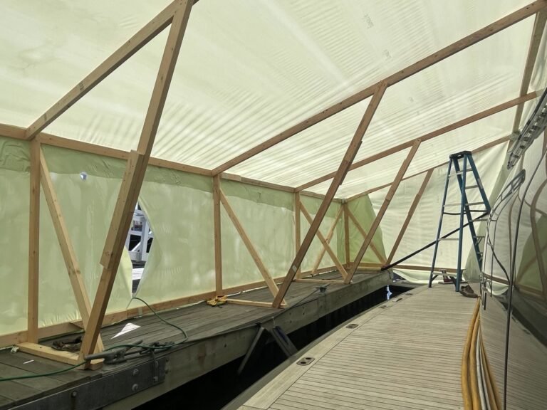 bioaqualife: A wooden frame structure covered with translucent plastic sits on a dock beside a boat; a blue ladder stands inside the enclosure.