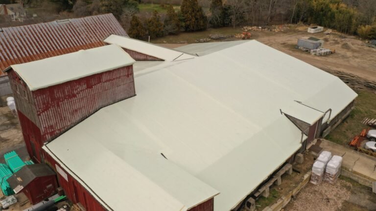 bioaqualife: A large barn-like building with a red exterior and a pale, light-colored roof sits on a rural property with scattered construction materials and trees in the background.