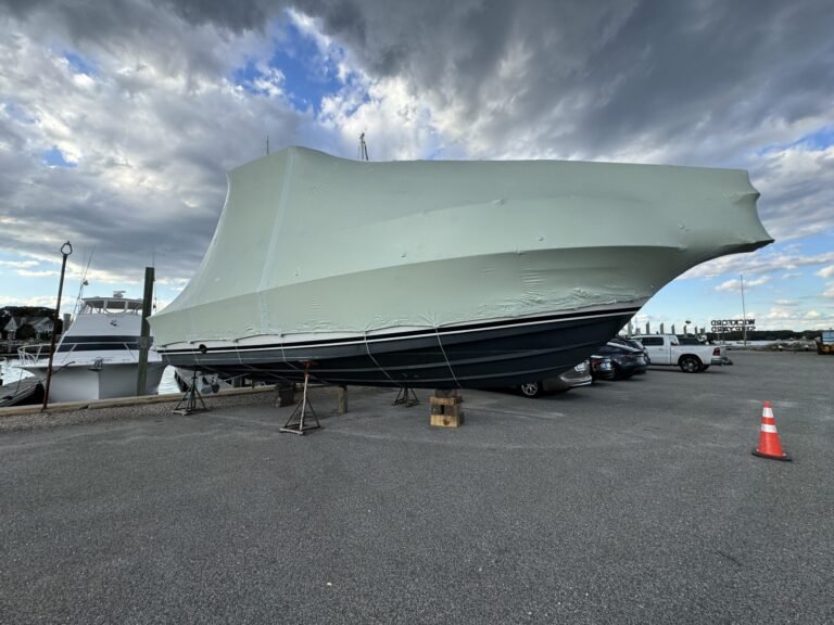 bioaqualife: A large boat covered in a protective wrap is propped up on stands in a marina parking lot, with a partly cloudy sky above and a traffic cone nearby.